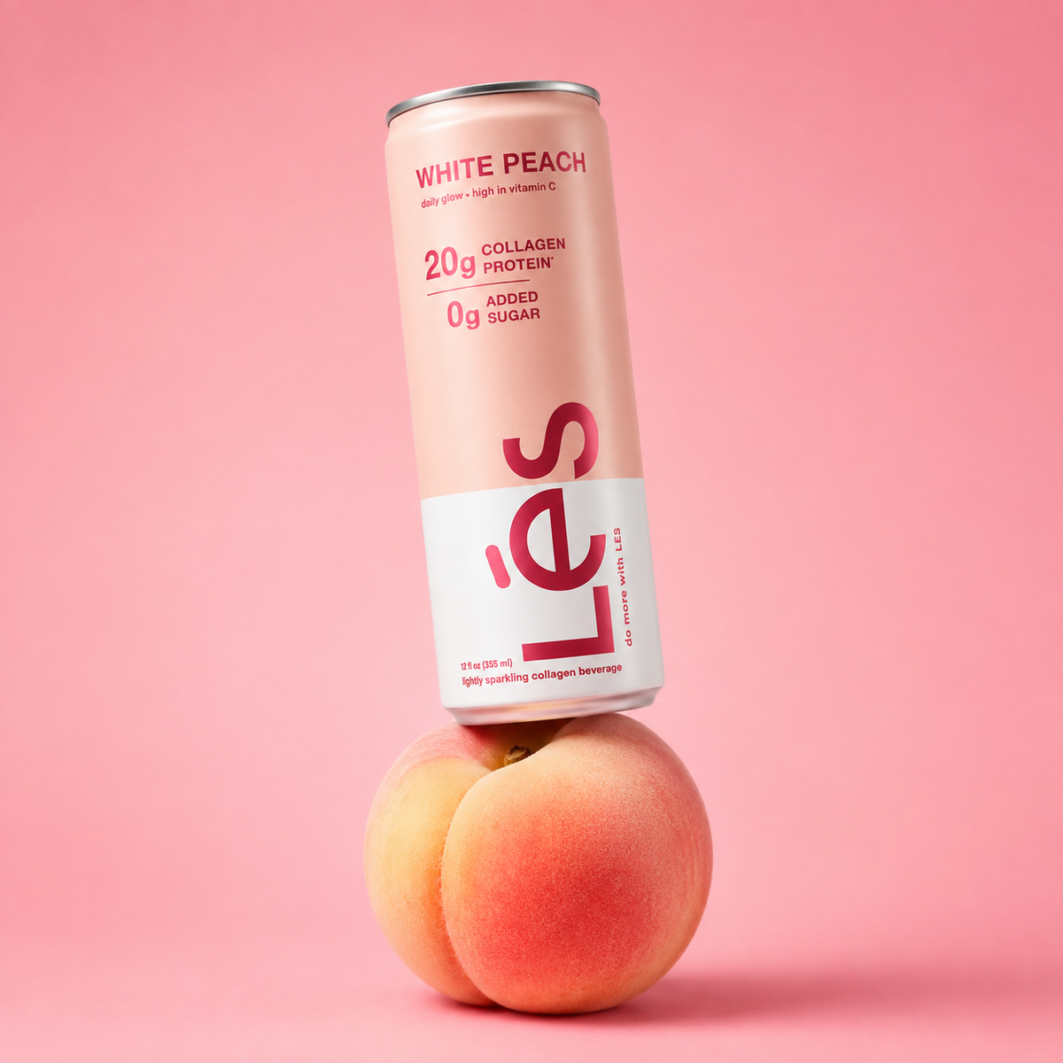 LÉS White Peach sparkling collagen protein drink, pink can resting on two fresh peaches. Can reads 20g collagen protein, 0g added sugar.